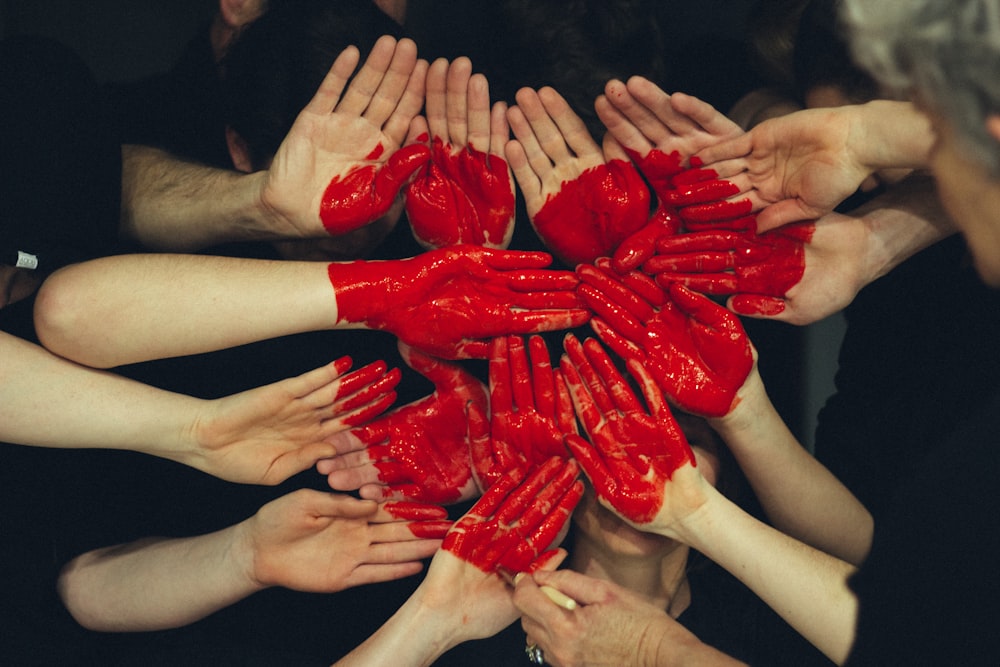Many people's hands are painted red to form together a large red heart