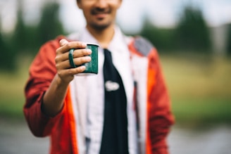 A person wearing a Rush Coffee branded sweatshirt, holding a mug outdoors.