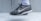 A close-up view of a black and white athletic shoe with a prominent swoosh logo on the side. The shoe is being worn with a white athletic sock, and it appears to be in a mid-air position against a light grey background.
