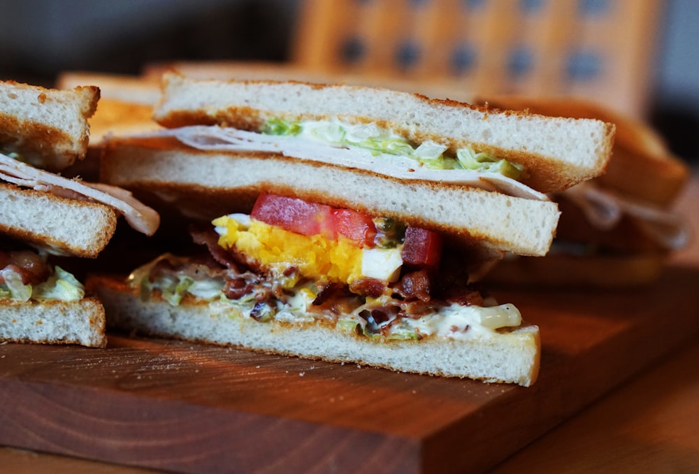 A club sandwich with tomato, lettuce, egg, bacon, mayonnaise, and turkey on a wooden plate