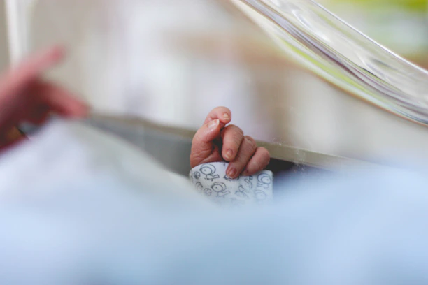 Close-up of a tiny baby hand clutching a soft, mint green lulliva swaddle.