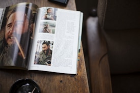An open magazine rests on a wooden surface, displaying a series of photographs and a lengthy article. The visible page shows several images of a man smoking a cigar, presumably from various points in his life, accompanied by text. The background includes a corner of a chair and an ashtray with a cigar stub on the table.