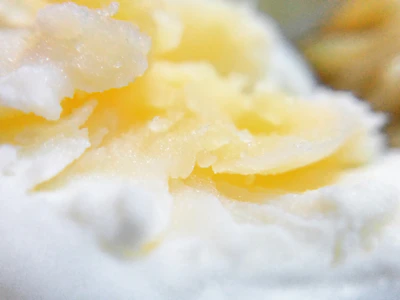 Close-up of rich, creamy shea butter being scooped from a jar, highlighting its smooth texture.