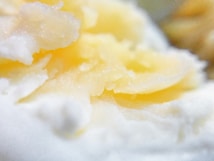 Close-up of a buttery texture with soft, creamy folds. The focus is on the smooth and rich consistency, hinting at a freshly spread or carved, pale yellow material, surrounded by a lighter, airy substance.