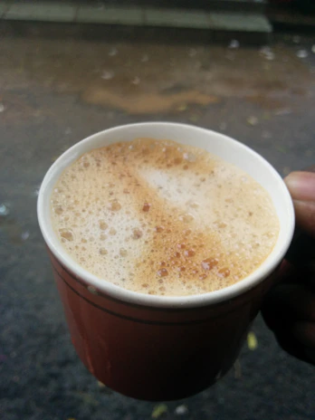 Close-up of a hand holding a steaming cup of coffee with blurred cityscape background.