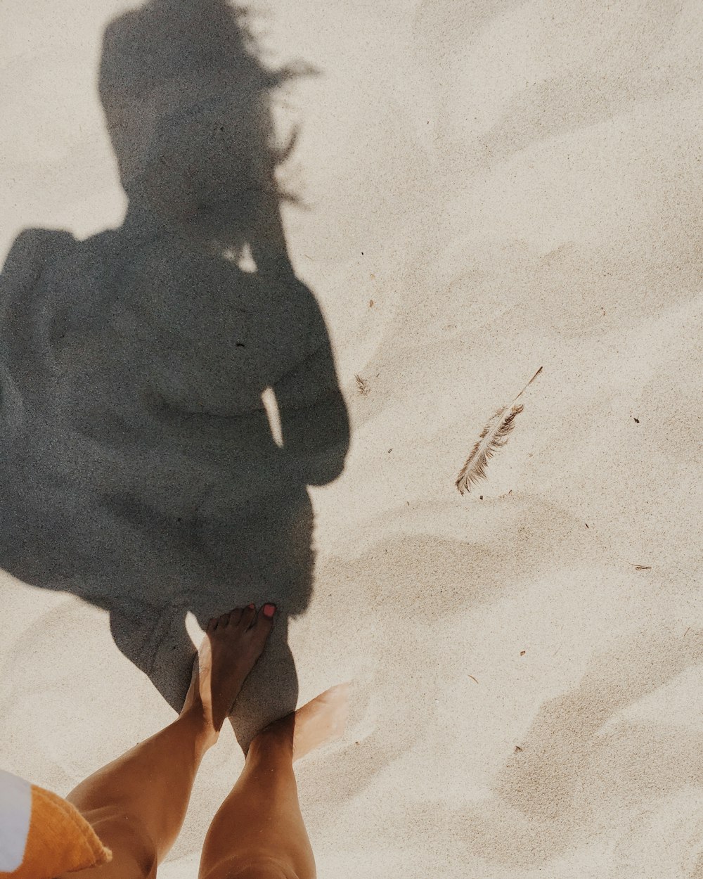 The shadow of a woman standing in the sand on a beach.