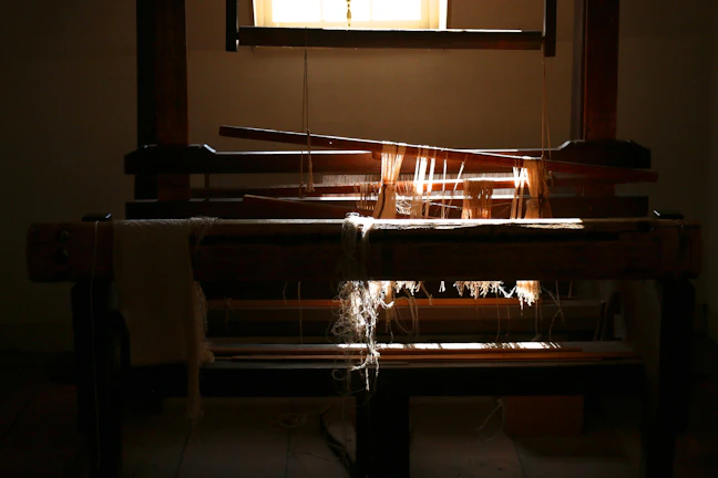A close-up of hands weaving colorful yarn on a vintage loom bathed in warm afternoon light.