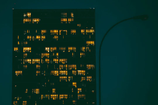 Night view of a modern high-rise residential building illuminated with warm lights against a dark sky.
