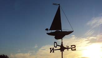 A vintage-style sailboat weathervane spinning gently against a clear blue sky.
