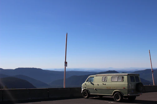 Photo of a vintage blue van parked beside a scenic mountain road.