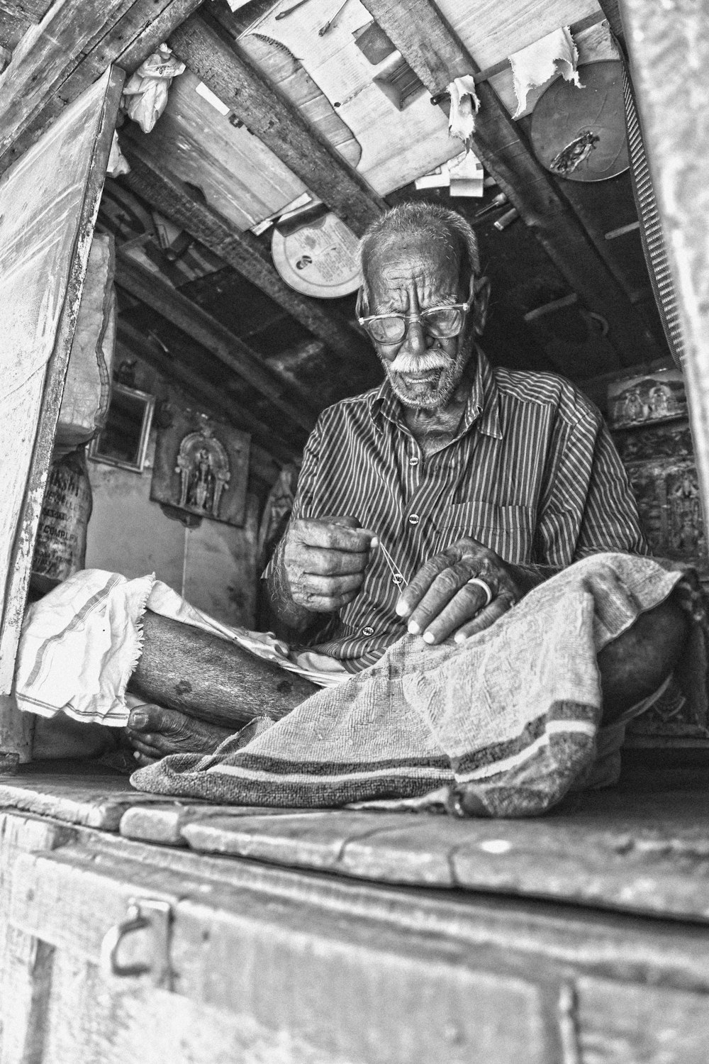 grayscale photo of man sewing textile while sitting on floor