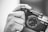 A black and white image featuring a close-up of a hand holding a vintage Yashica camera. The word 'click' is tattooed across the finger, adding an artistic touch to the composition.