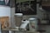 A kitchen shelf holds a few appliances and utensils. There is a blender with its jar placed next to a traditional kettle labeled 'HOT.' A glass beverage pitcher is present, alongside a bamboo drying rack for utensils. Above, a chalkboard with artistic lettering reads 'Artwork.' The setting has an eclectic and vintage aesthetic, partly due to the kitchen’s aged decor and utensils.