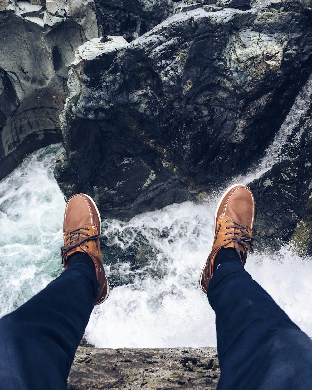 바위 가장자리에 앉아 흐르는 물의 사진을 찍는 사람