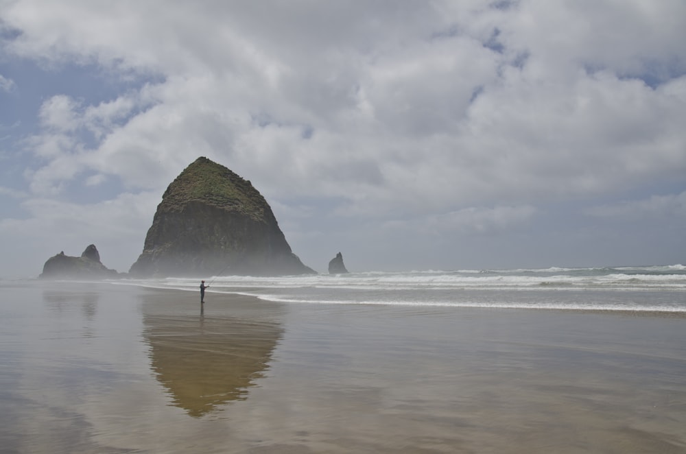 person standing on seashore with hill