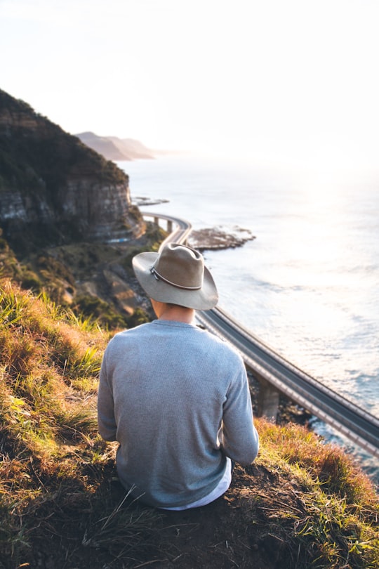 person sitting on cliff in Sea Cliff Bridge Australia