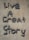 Letters formed with small, round stones on a sandy-colored surface spell out the phrase 'Live A Great Story'.