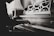 A person is playing a piano with a sheet music stand in the background. The scene appears to be indoors, with soft lighting casting shadows on the instrument and the musician's hands. The image is in black and white, highlighting the intricate details of the piano's wood texture.