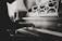 A person is playing a piano with a sheet music stand in the background. The scene appears to be indoors, with soft lighting casting shadows on the instrument and the musician's hands. The image is in black and white, highlighting the intricate details of the piano's wood texture.