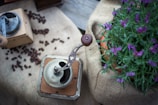 A vintage-style manual coffee grinder next to a steaming cup of black coffee.