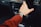 A hand wearing a smartwatch is reaching towards the dashboard of a car, with control dials and a display visible in the background. The person is wearing a long-sleeved red shirt.