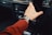 A hand wearing a smartwatch is reaching towards the dashboard of a car, with control dials and a display visible in the background. The person is wearing a long-sleeved red shirt.