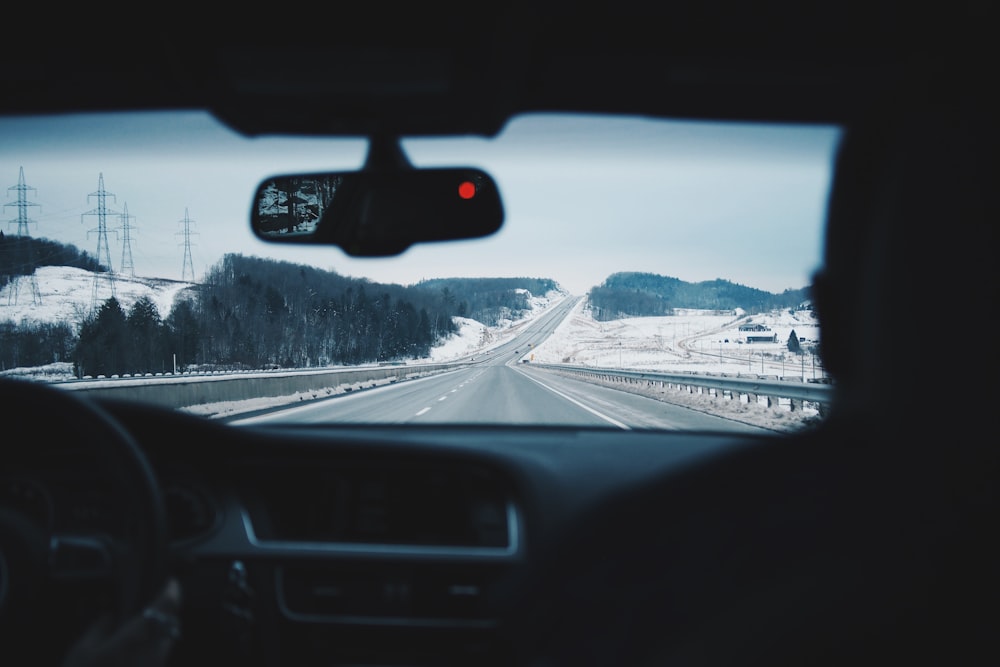 two people inside of car while driving on asphalt road between of land with covered of snow