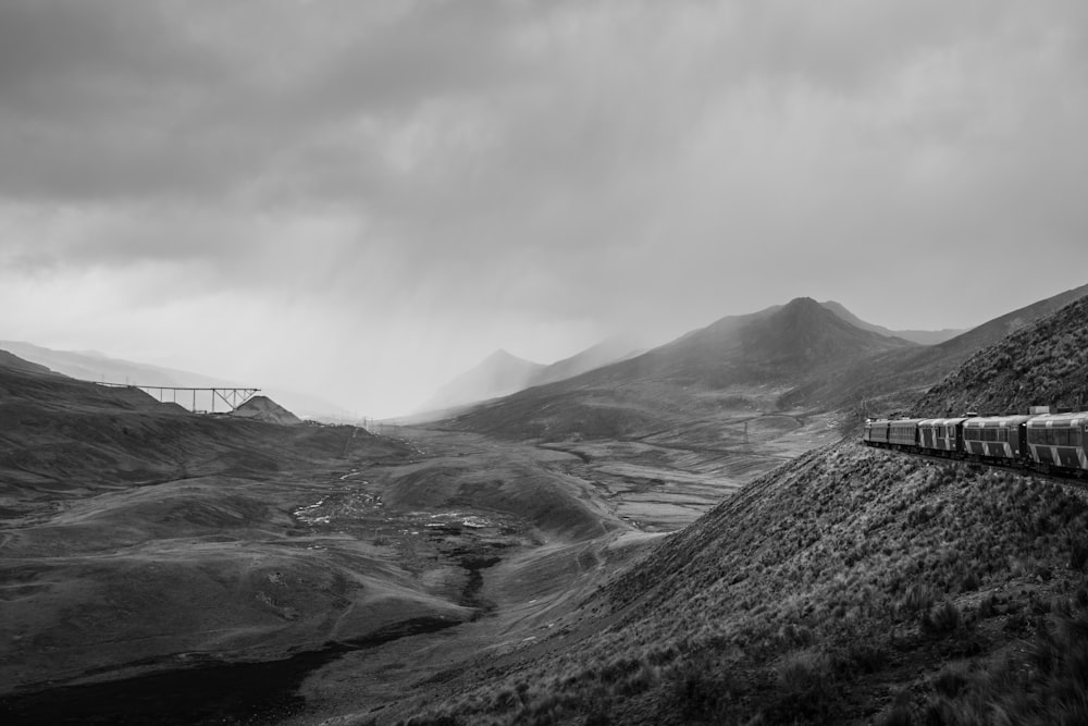 grayscale photo of train beside of mountain during cloudy sky