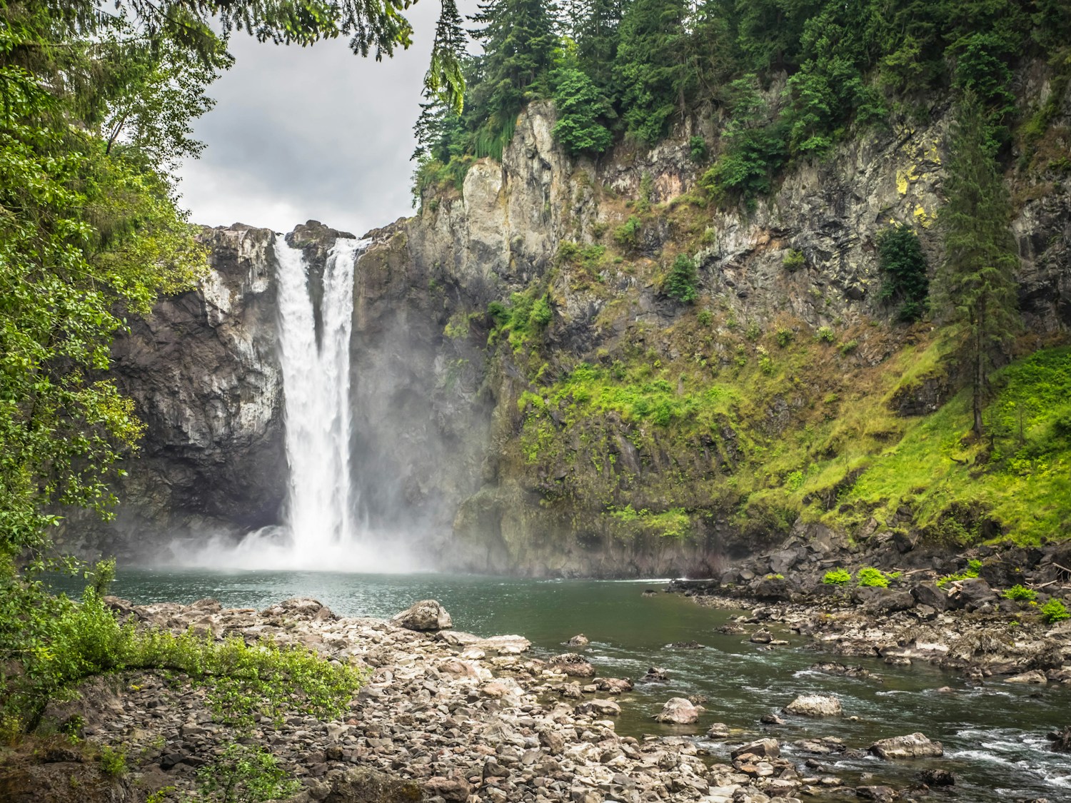 Snoqualmie Falls cascading between rocky cliffs and evergreen forest in Washington.
