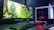 A sleek computer setup featuring a large monitor displaying a forest scene with vibrant greenery. Next to the monitor is a white tower with visible red lighting from internal components. A keyboard and mouse are placed in front, on a desk with a dark surface.
