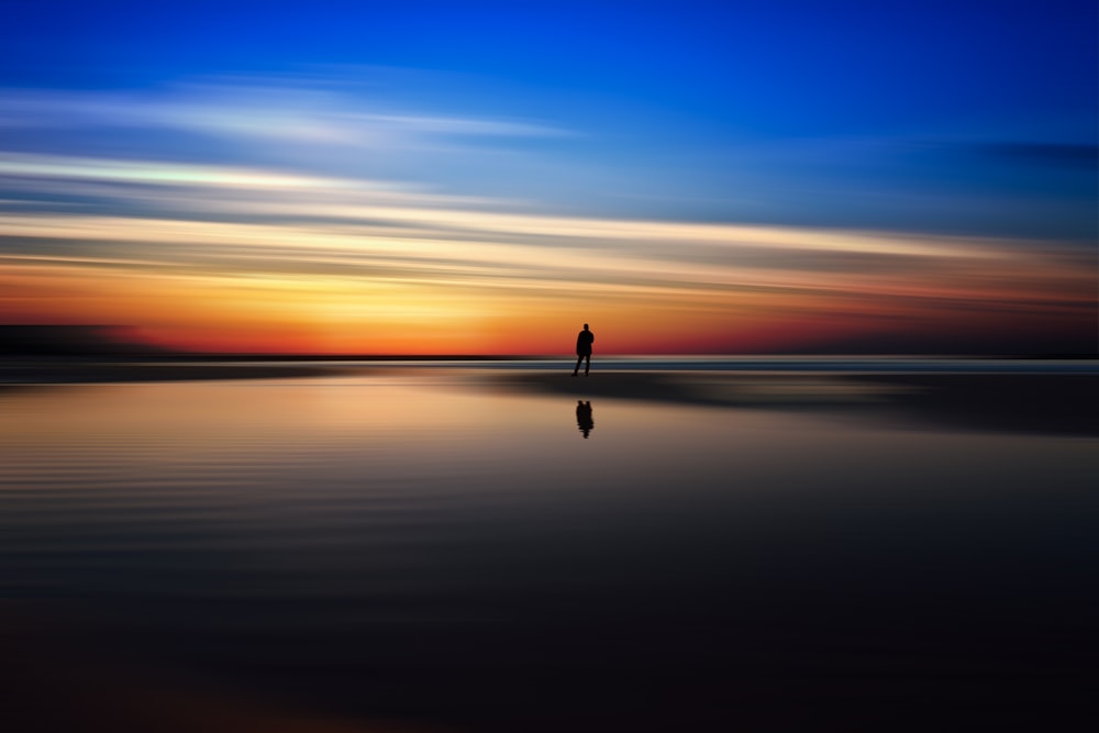 person standing in seashore under horizon