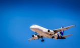 A commercial airplane flying against a clear blue sky, showcasing its aerodynamic design and landing gear. The aircraft is predominantly white with colorful branding on the tail and wings.
