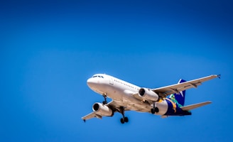 A commercial airplane flying against a clear blue sky, showcasing its aerodynamic design and landing gear. The aircraft is predominantly white with colorful branding on the tail and wings.
