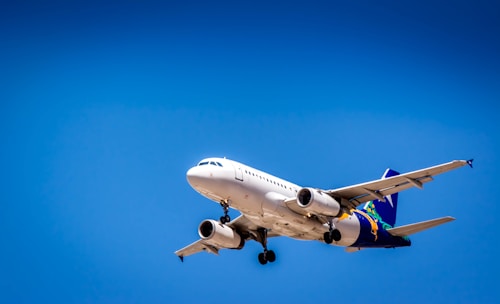 A commercial airplane flying against a clear blue sky, showcasing its aerodynamic design and landing gear. The aircraft is predominantly white with colorful branding on the tail and wings.
