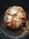 A rustic round loaf of bread with a golden-brown crust, dusted with flour and sitting on a dark baking sheet. The surface of the bread is cracked, giving it a homemade, artisanal appearance.