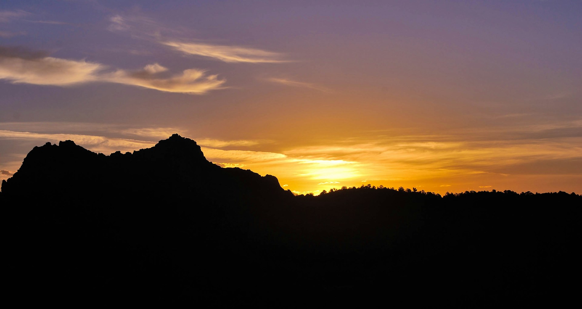 A stunning sunset over a mountain range, with warm hues reflecting off the peaks and a calm foreground.