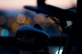 A blurred artistic photograph focusing on the silhouette of a bicycle's handlebar and headlight, with a backdrop of softly lit bokeh lights in warm tones.