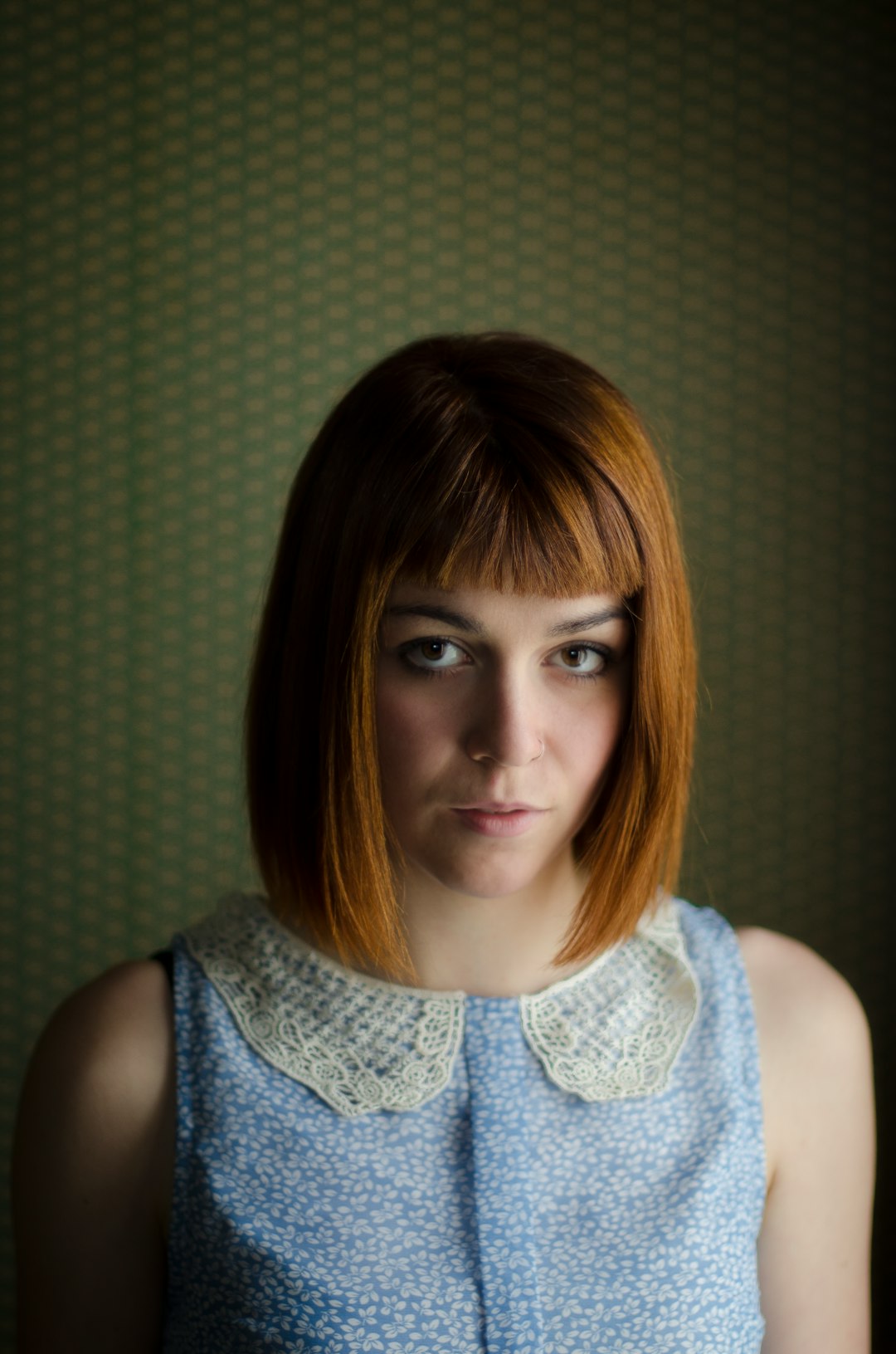 woman in blue floral sleeveless top in front of a wall