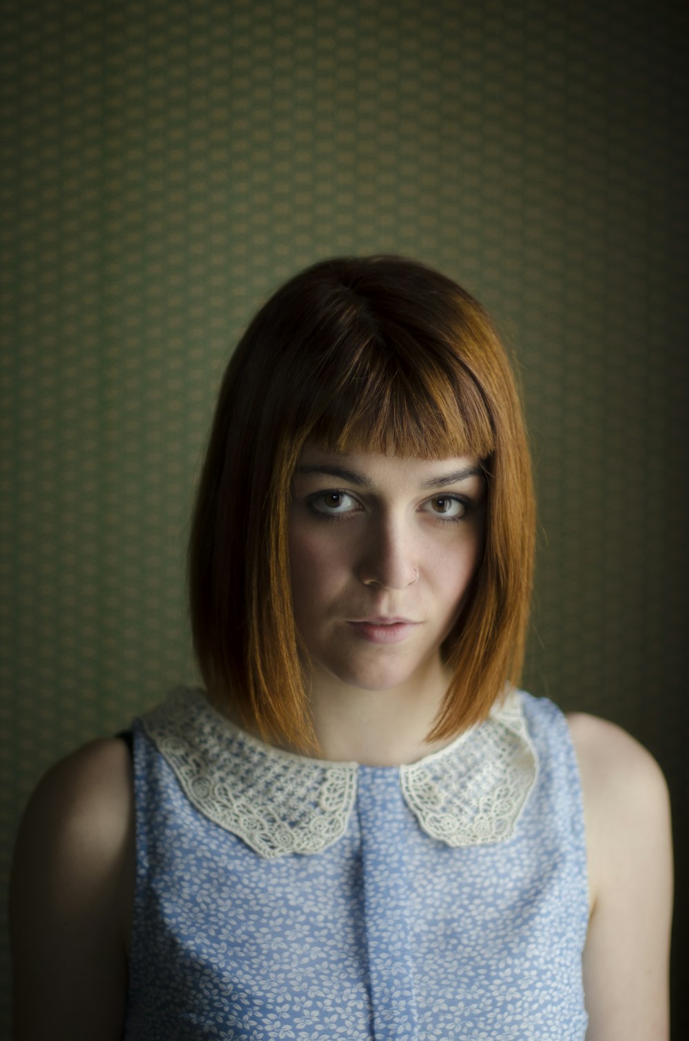 woman in blue floral sleeveless top in front of a wall