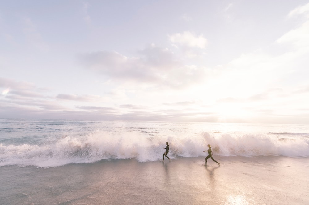 duas pessoas correndo na praia à beira-mar durante o dia