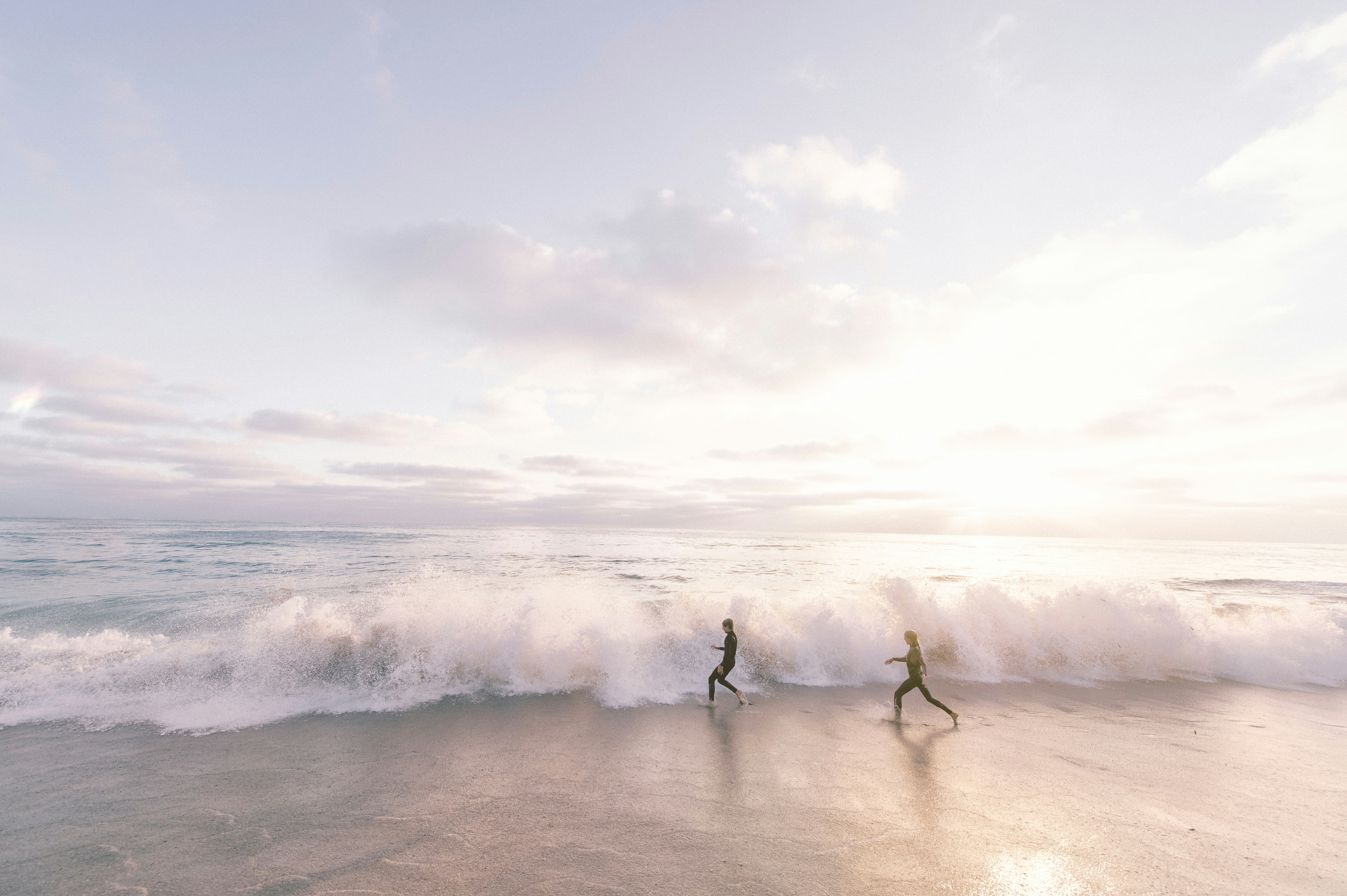 two person running on seaside beach during daytime