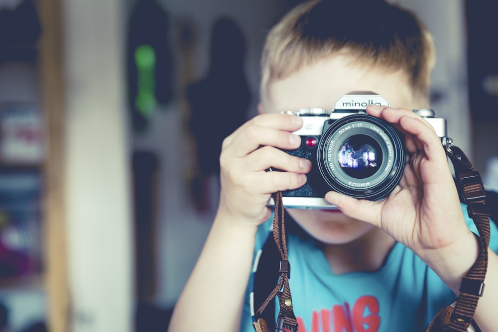 selective focus photography of boy holding gray Minolta bridge camera