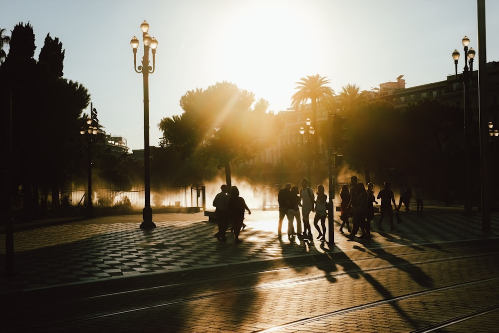 Silhouettes of pedestrians on the streets of Nice, as the sun sets behind palm trees in the distance