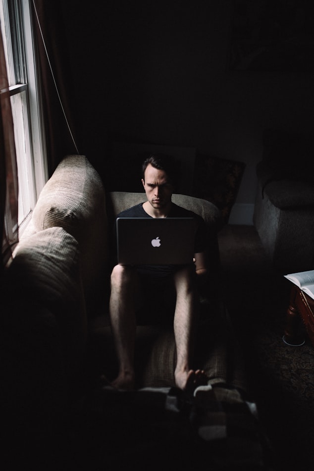 皺眉頭的男子在黑暗房間的沙發上用蘋果電腦
