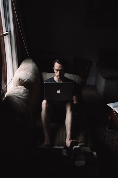 Man seating on sofa using MacBook beside window