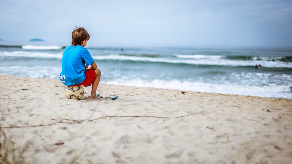 menino sentado na bola enquanto olha para o oceano