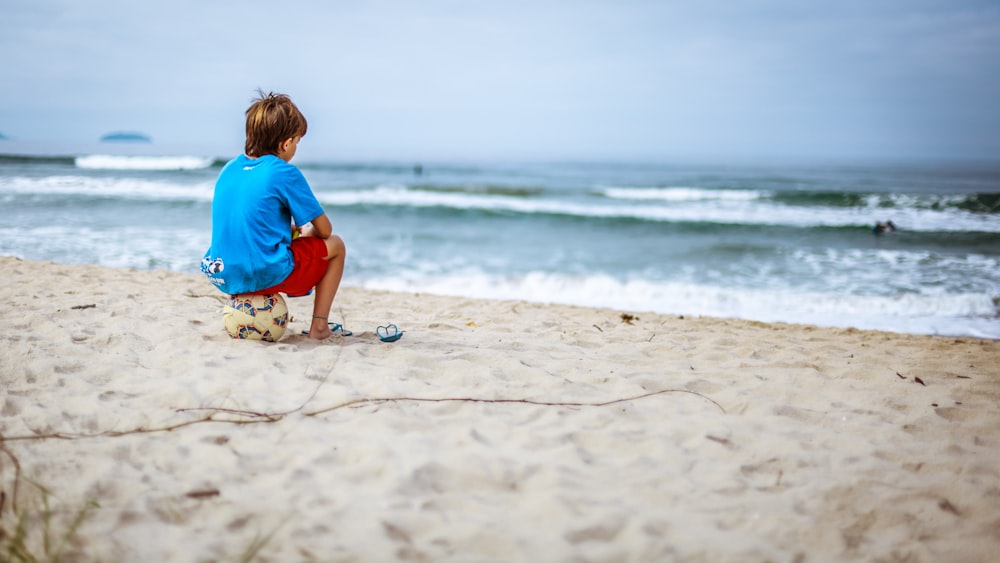 ragazzo seduto sulla palla mentre fissa l'oceano