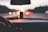 View from inside a car, focusing on the dashboard and a hanging air freshener, with an out-of-focus road and cars in the background. The dashboard's speedometer is partially visible, and the interior is dimly lit, suggesting evening or nighttime. The bokeh effect in the background creates a sense of motion.