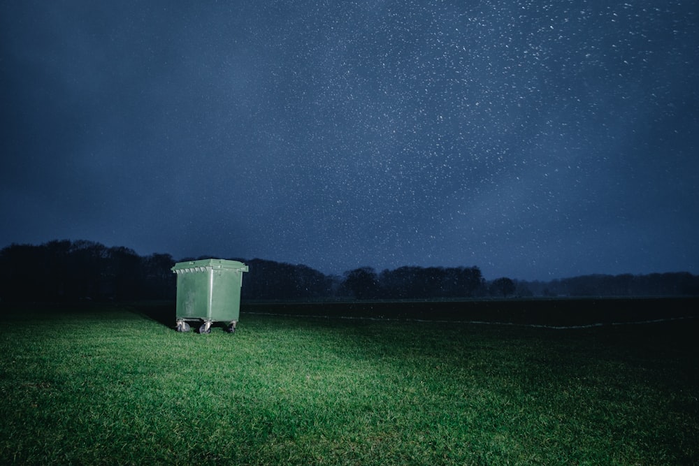 A garbage can sitting in a field under a starry night sky.