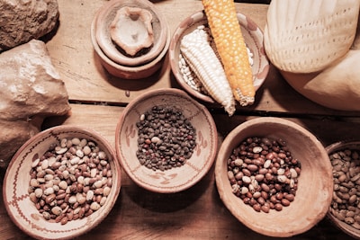 Variety of dry seeds and beans displayed in rustic bowls on a wooden table.